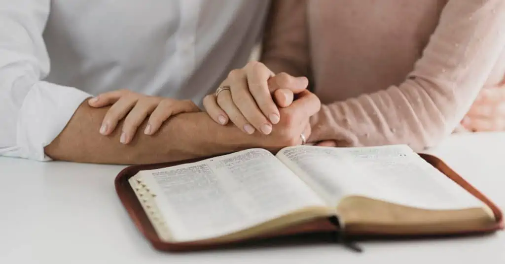 Couple Holding Hands and Reading the Bible
