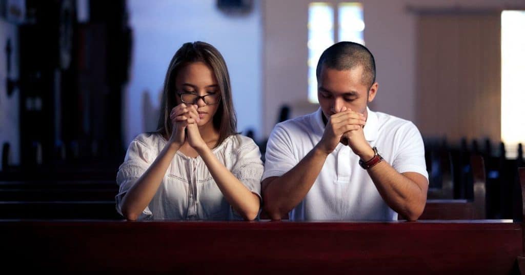 Woman and man next to each other kneeling and praying in church