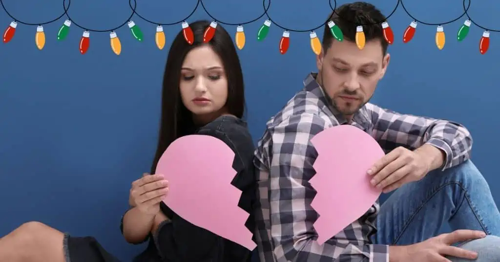 Man and woman sitting back to back each holding half of a broken heart with Christmas lights above them