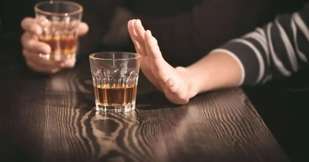 womans hand pushing away a shot of alcohol with man holding shot of alcohol in background