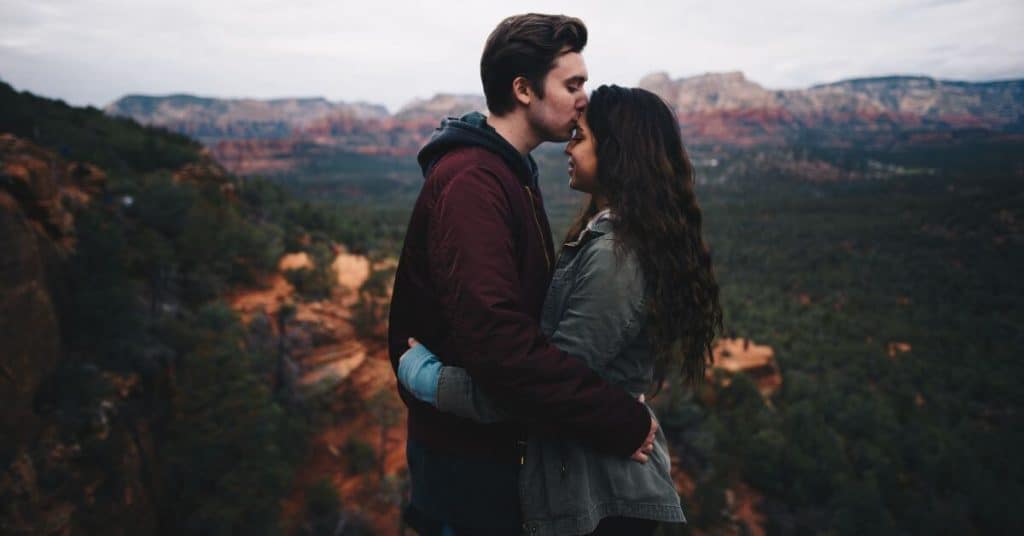 Man kissing woman's forehead on moutain top